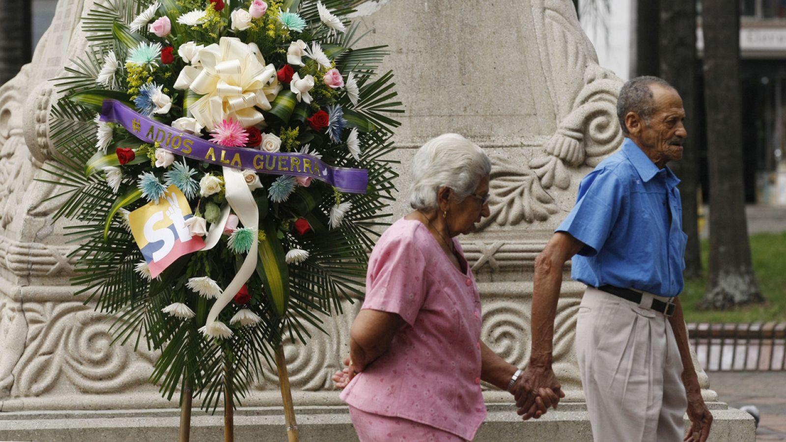 Una pareja de ancianos camina en Cali, Colombia, frente a una corona fúnebre con el rótulo "Adiós a la guerra"