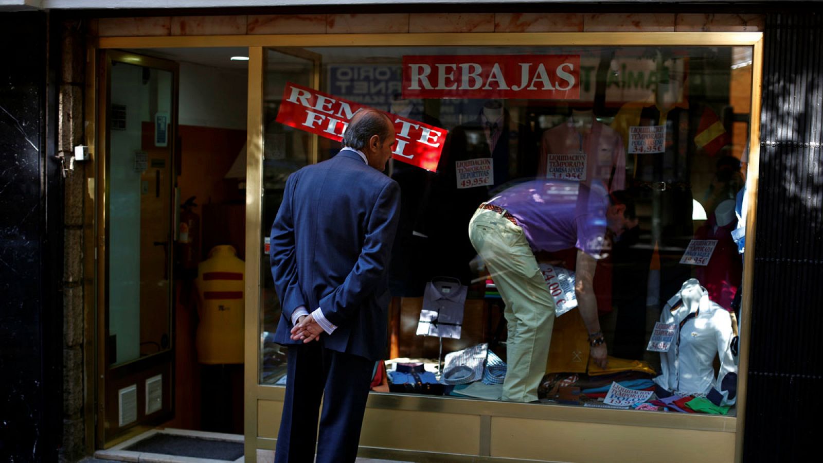 Un hombre cambia el letrero de las rebajas en un escaparate