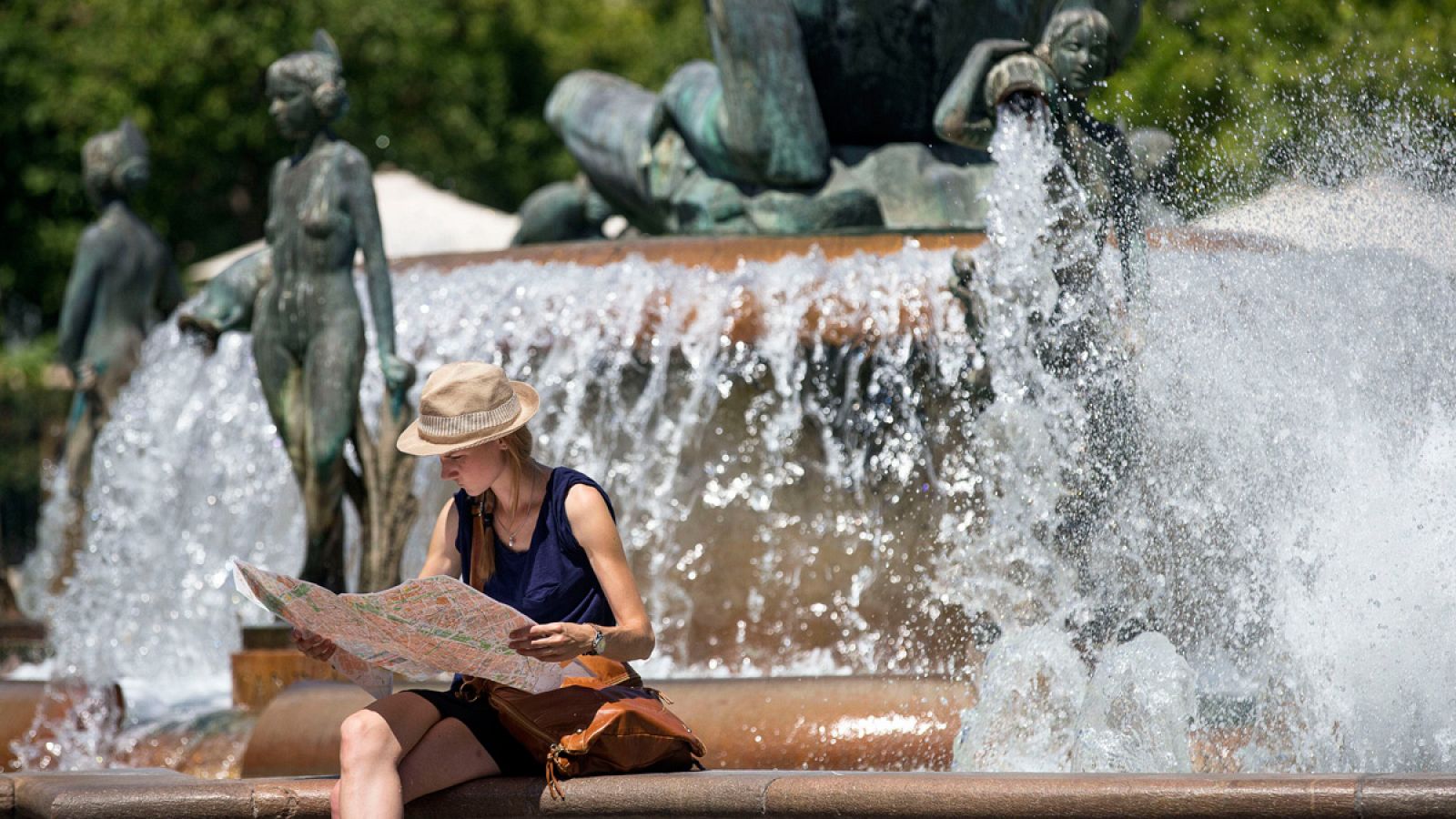 Una joven turista consulta un mapa de la ciudad sentada en la céntrica fuente de la plaza de la Virgen de Valencia