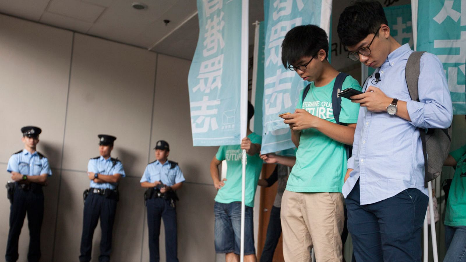Los activistas estudiantiles Joshua Wong (i) y Nathan Law (d)  miran sus moviles mientras esperan su sentencia en el exterior del tribunal.