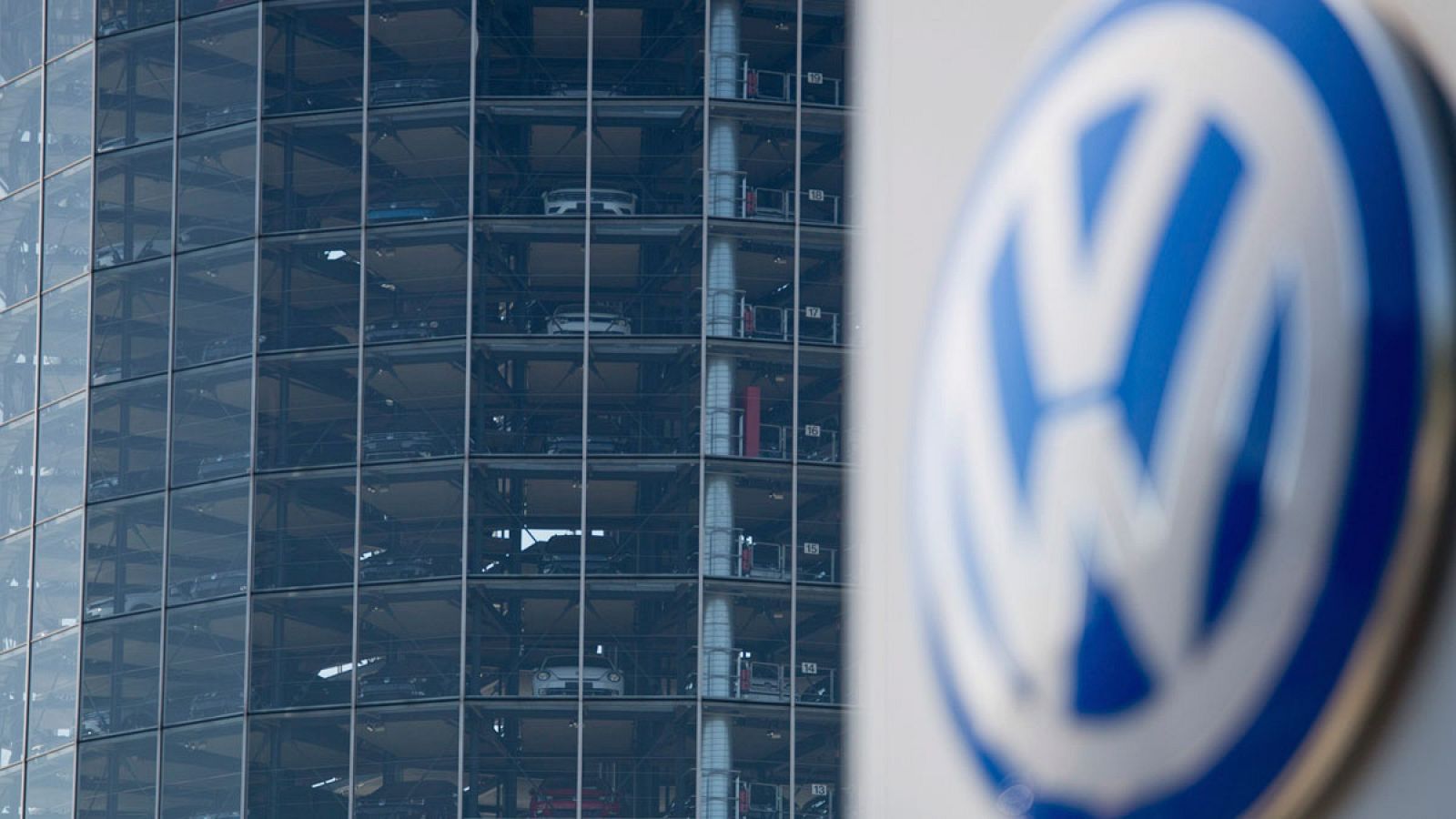 Vista del logo de Volkswagen delante de un edificio lleno de vehículos nuevos en una planta de Volkswagen en Wolfsburgo