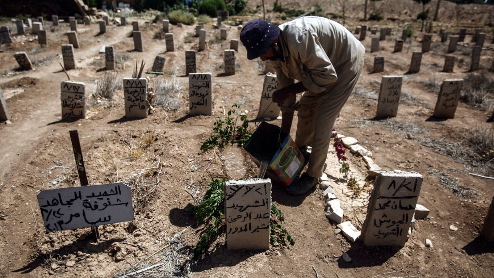 Fotografía de un hombre regando las flores depositadas en las tumbas de las víctimas del ataque químico en la localidad de Guta, en Siria, del pasado 21 de agosto de 2013 en el tercer aniversario de la masacre.