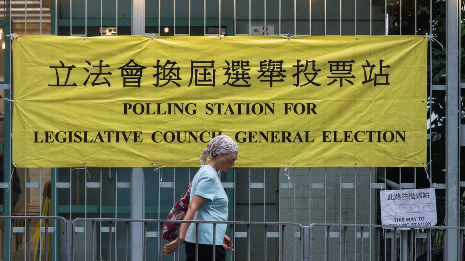 Una mujer camina frente a un cartel de un colegio electoral en Hong Kong.