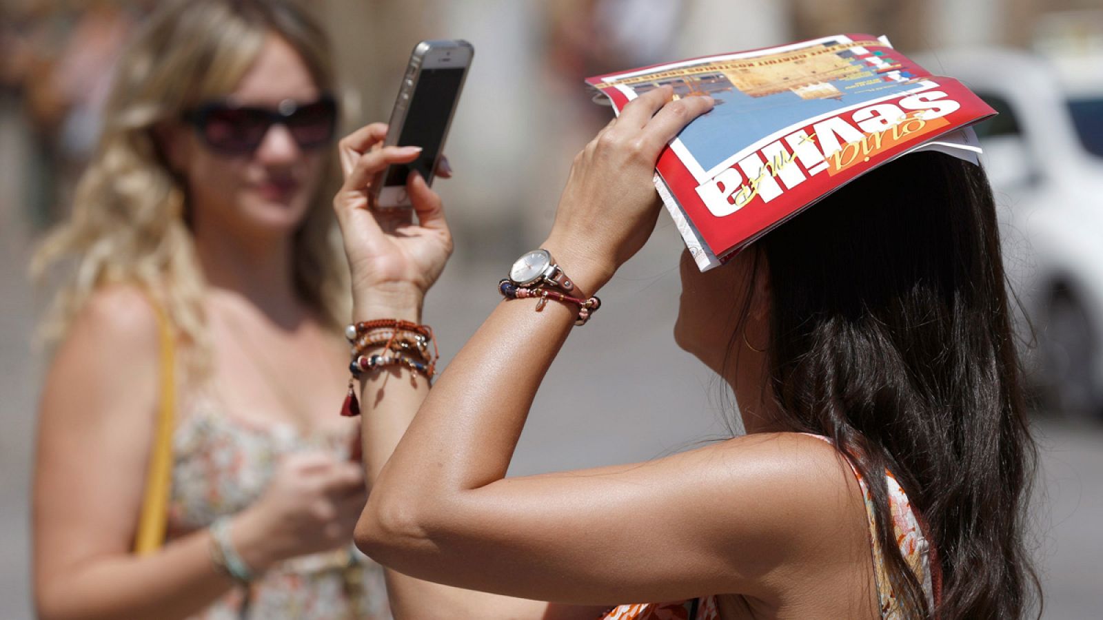 Una turista se fotografía con su teléfono móvil mientras se proteje del sol con una guía turística de Sevilla