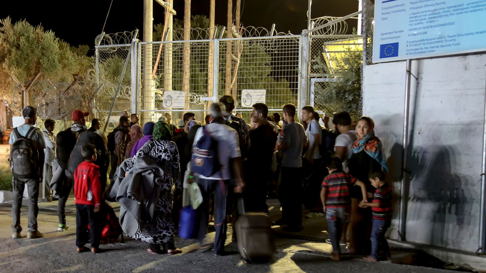 Refugiados y migrantes aguardan junto a una salida alambrada y cerrada en el campamento de Moria en Lesbos