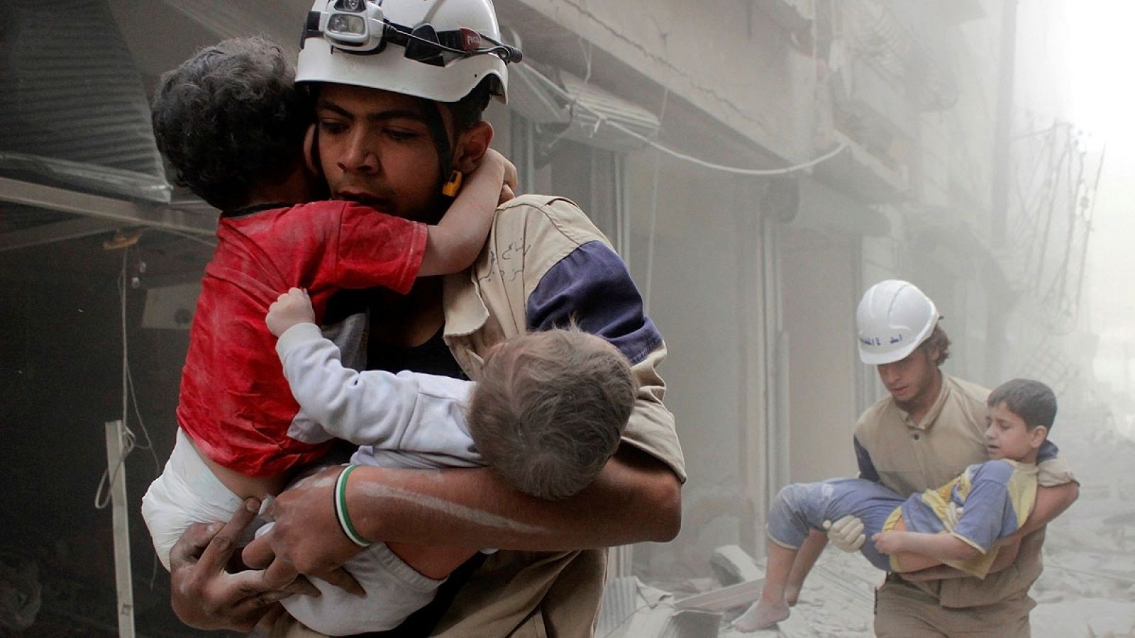 Dos hombres rescatan a varios niños tras un bombardeo de las tropas sirias en Alepo