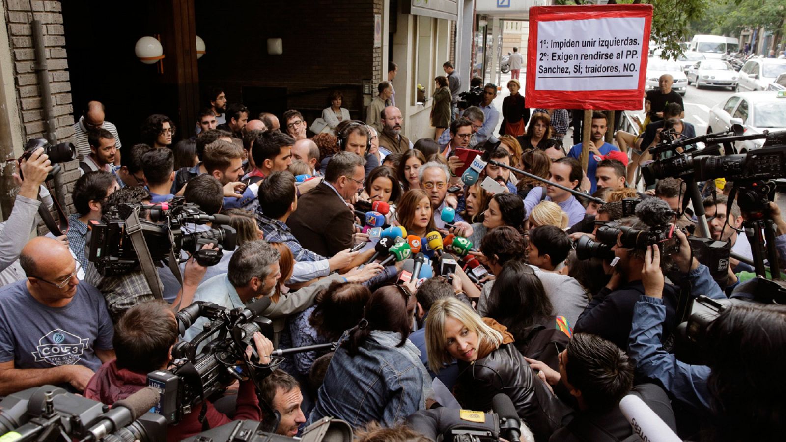 Una pancarta favorable a Pedro Sánchez se deja ver entre una nube de periodistas en la sede del PSOE.