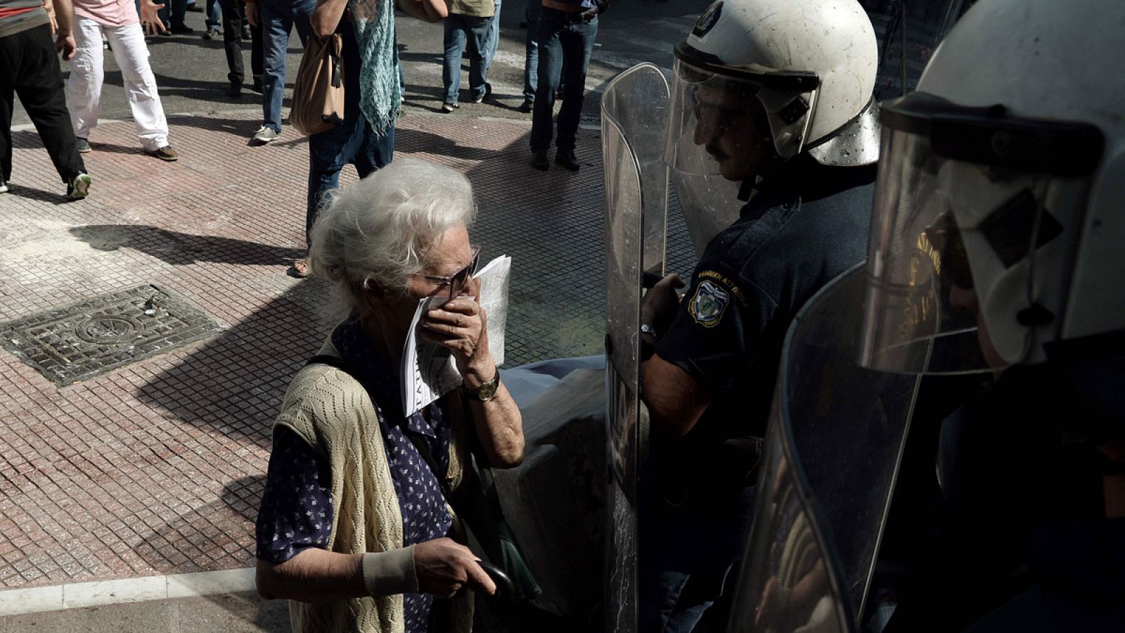 Una pensionista griega intenta respirar a través de un pañuelo frente a los antidisturbios