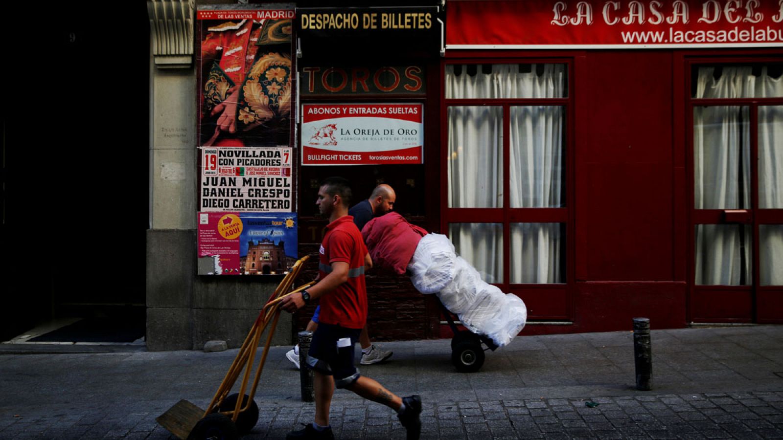 Dos operarios trasladan mercancía con carretillas en el centro de Madrid