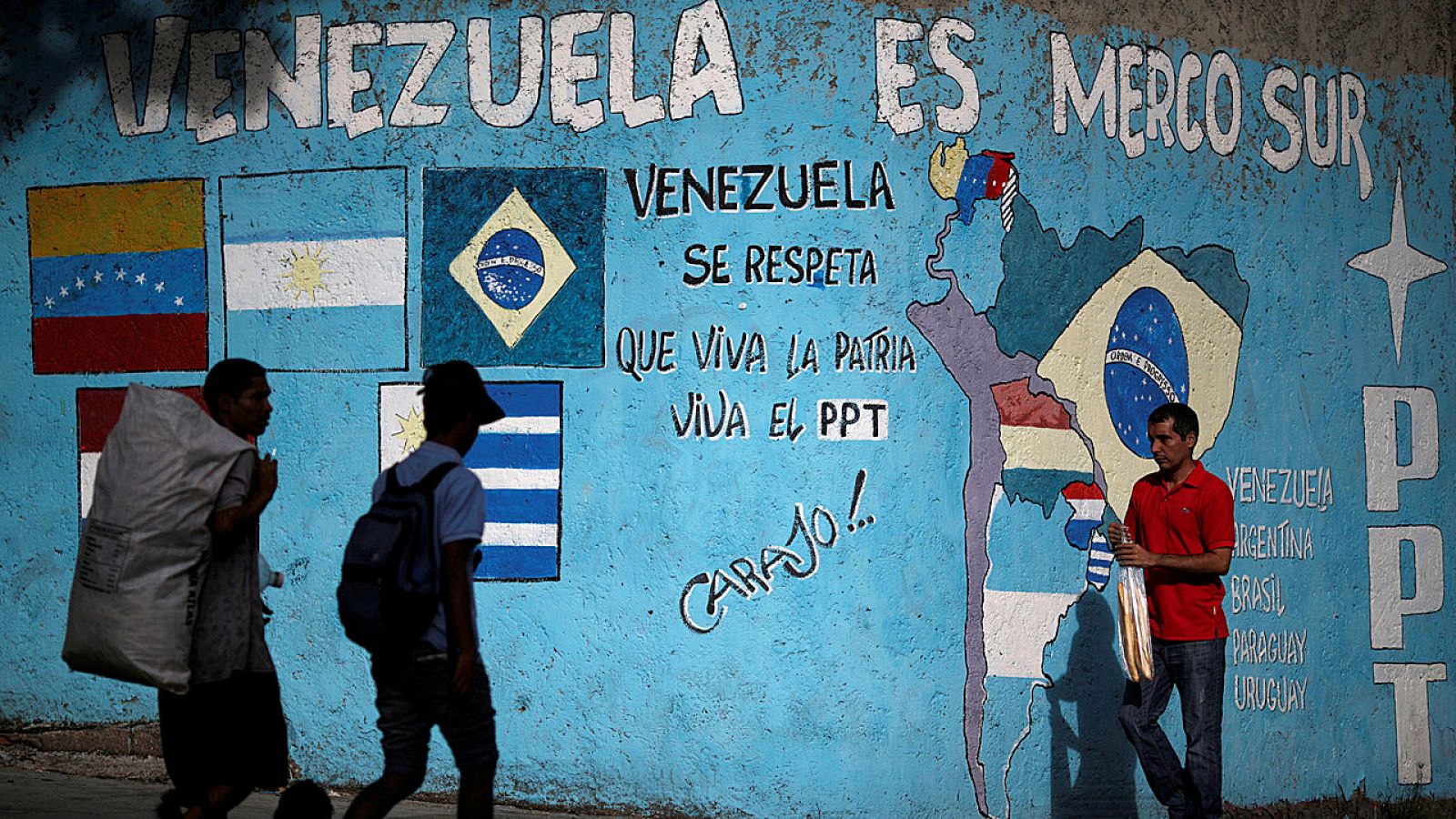 Ciudadanos venezolanos caminan en Caraas al lado de un mural que hace referencia a Mercosur.