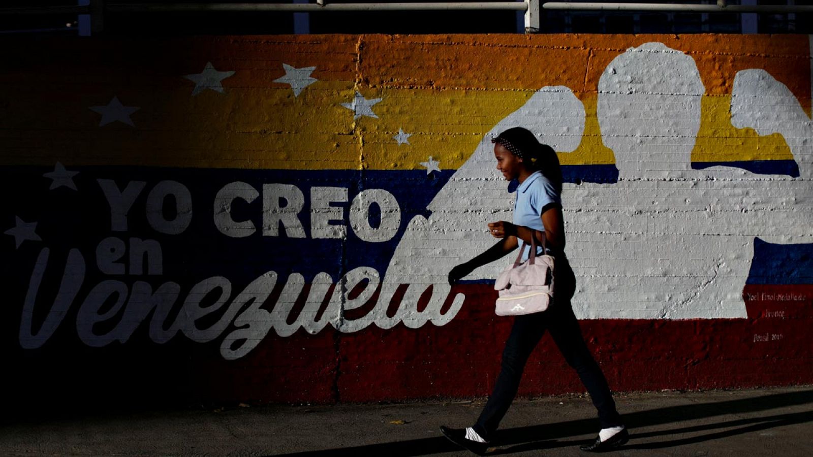 Una muchacha pasa ante un mural de Caracas que reza: "Creo en Venezuela"