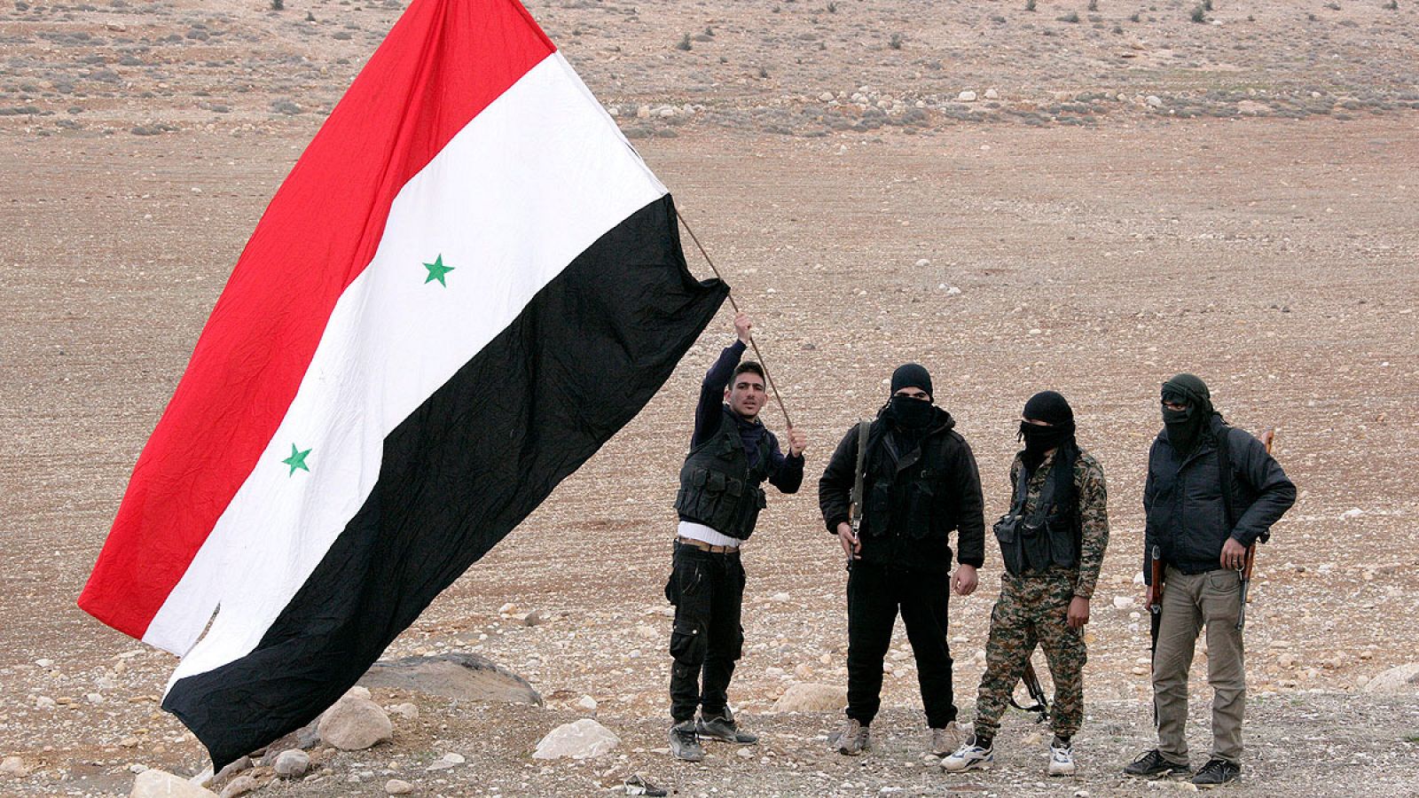 Hombres sirios armados ondean una bandera siria mientras esperan para registrar sus nombres y entregar sus armas a las autoridades