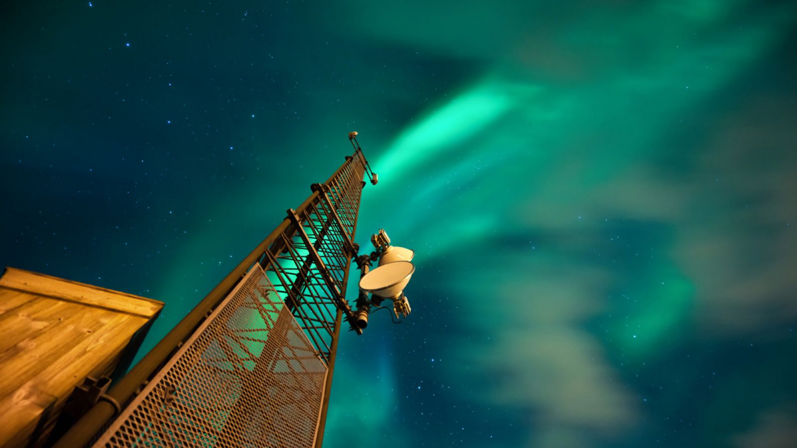 Una torre de telecomunicaciones iluminada por una aurora boreal