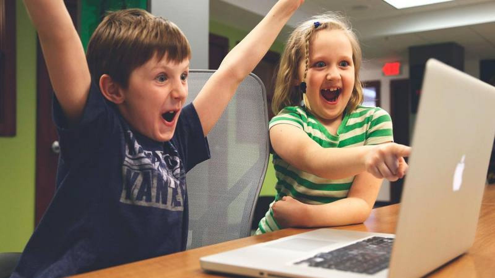 Un niño y una niña hacen gestos de alegría jugando a un videojuego por ordenador