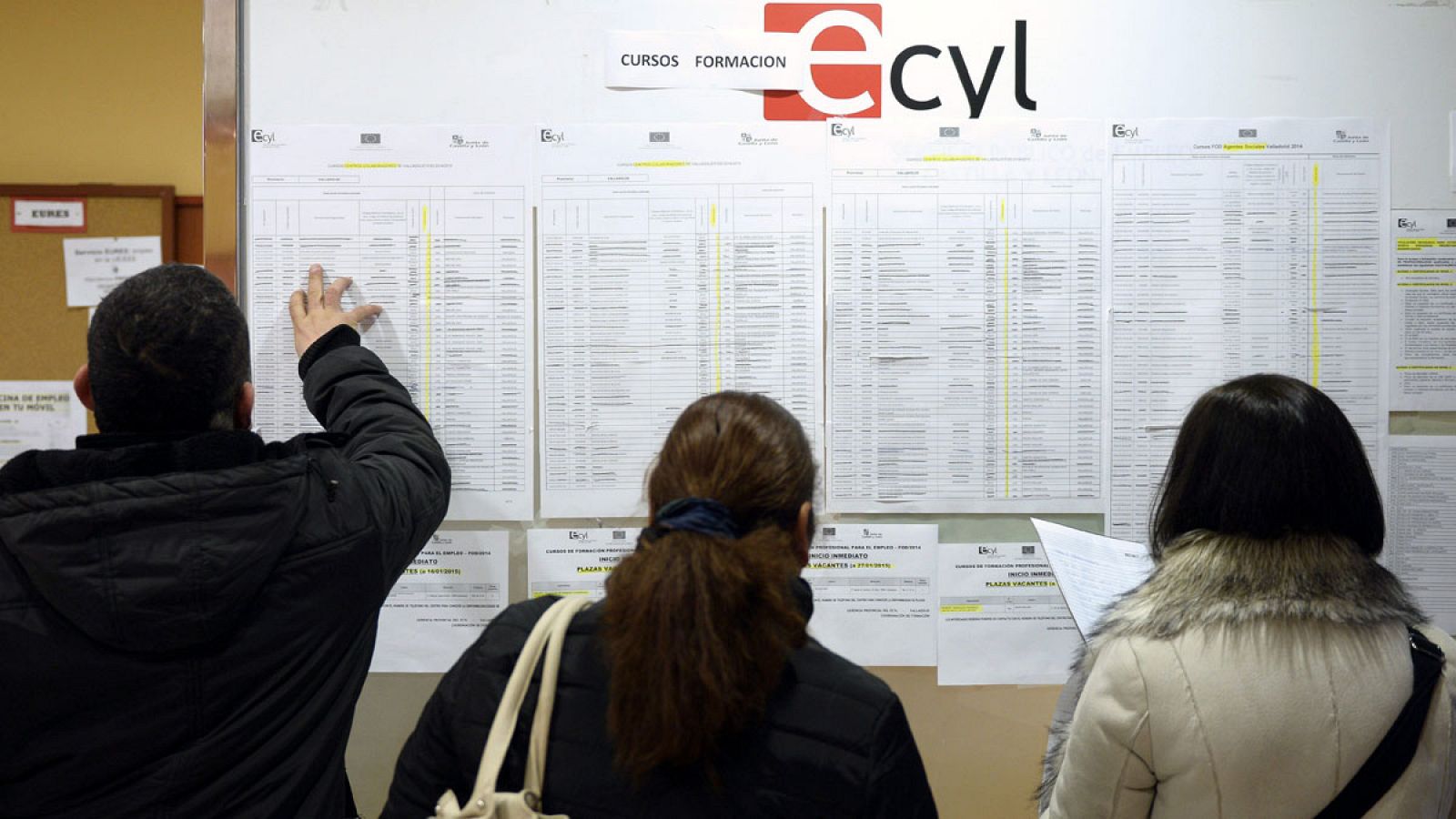 Tres personas consultan la información expuesta en una oficina de empleo de Valladolid.