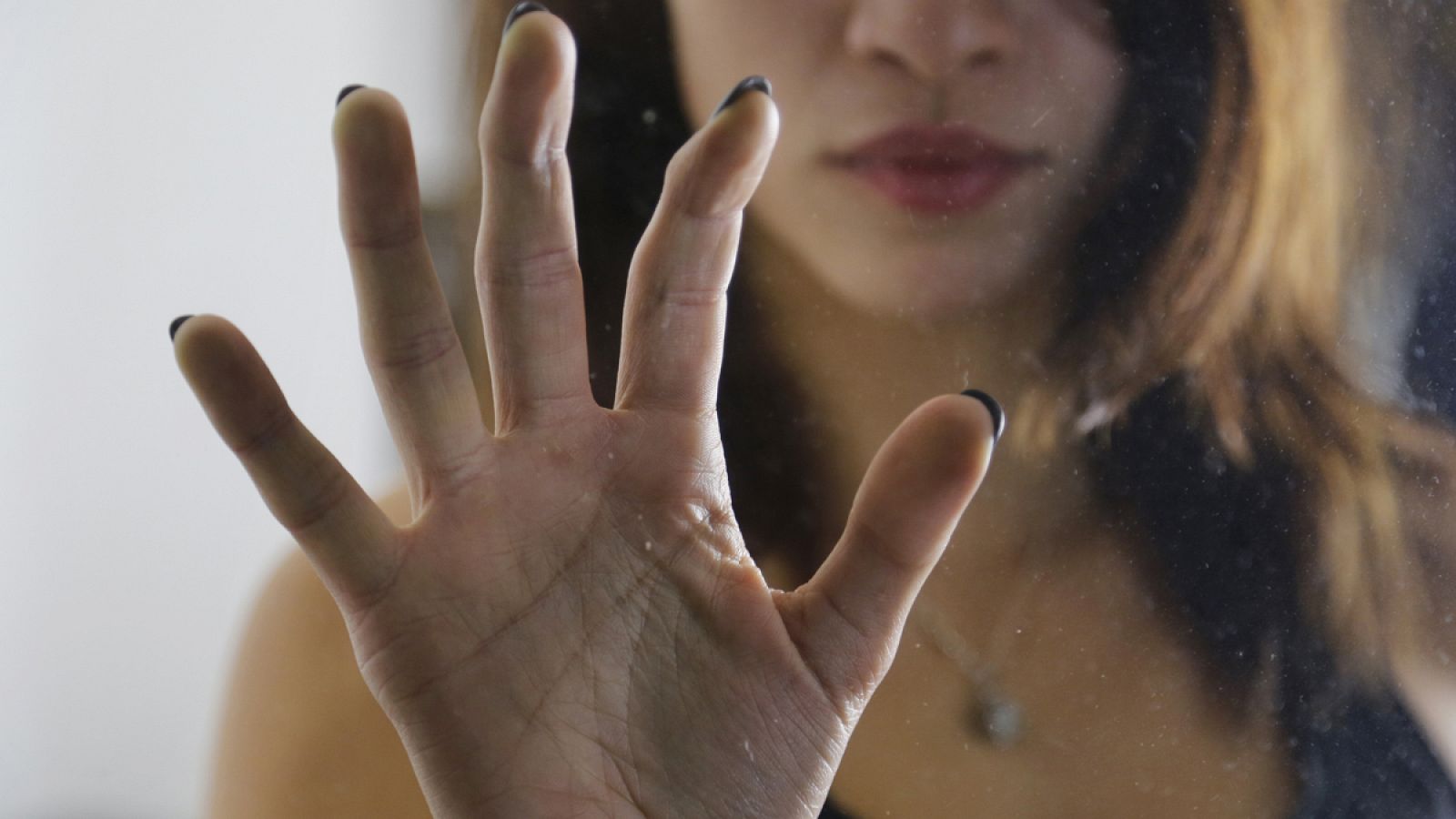 Una mujer apoya su mano en un cristal.