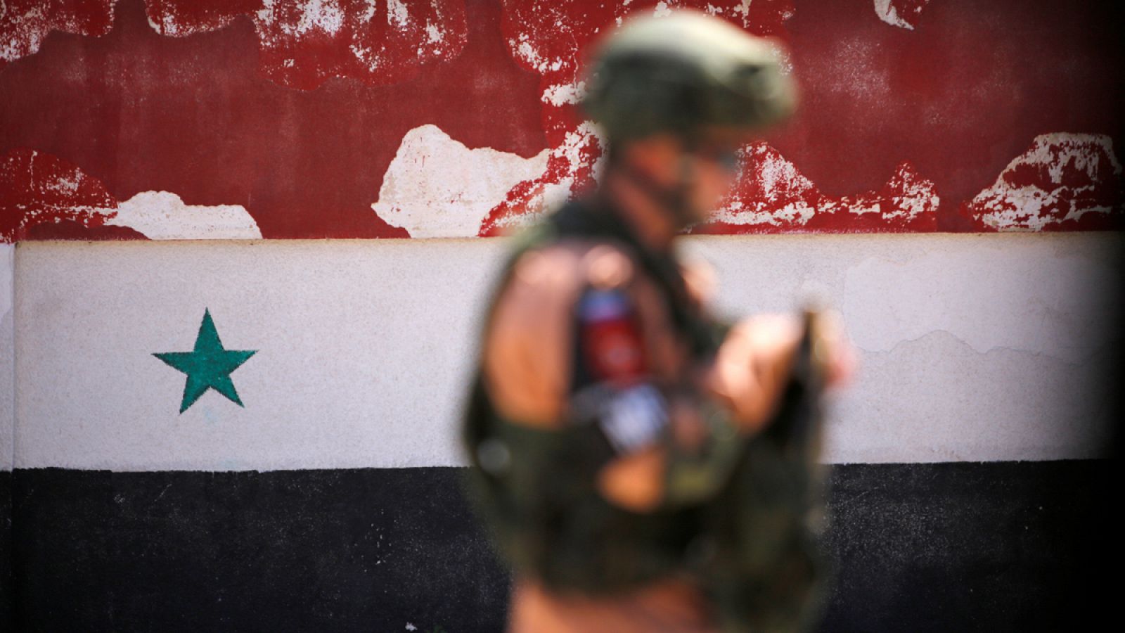 Un soldado patrulla frente a una bandera pintada en un muro en el barrio Al Waer, en Homs.