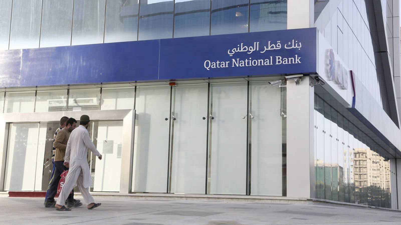 Hombres pasan frente al Banco Nacional de Catar en Riad, Arabia Saudí
