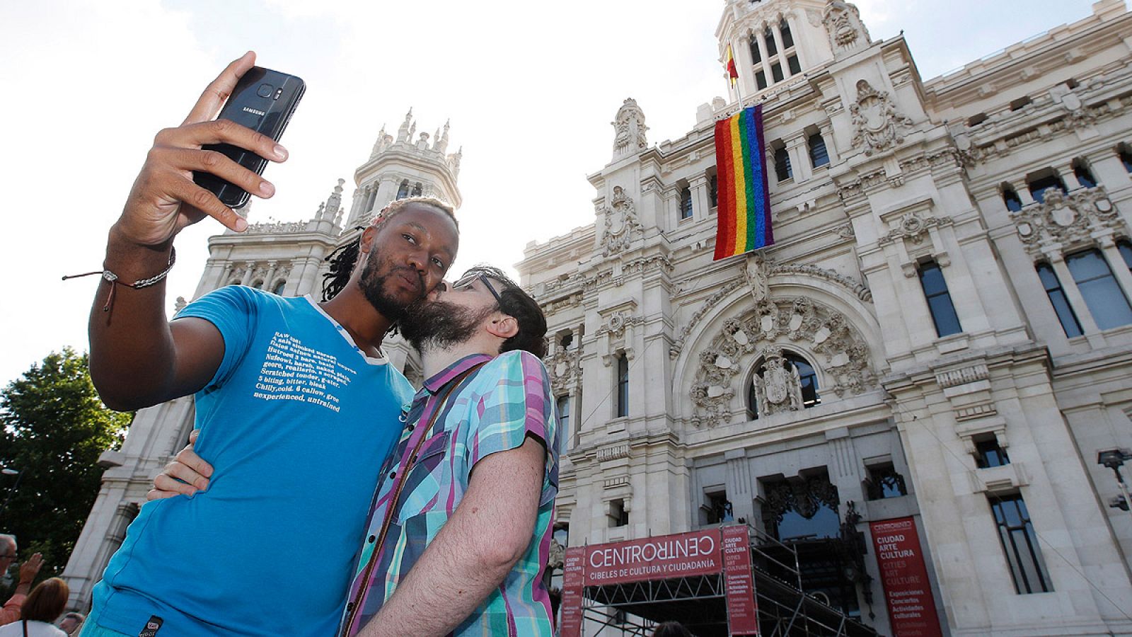 Una pareja se fotografía junto a la fachada del Ayuntamiento de Madrid con la bandera del orgullo gay