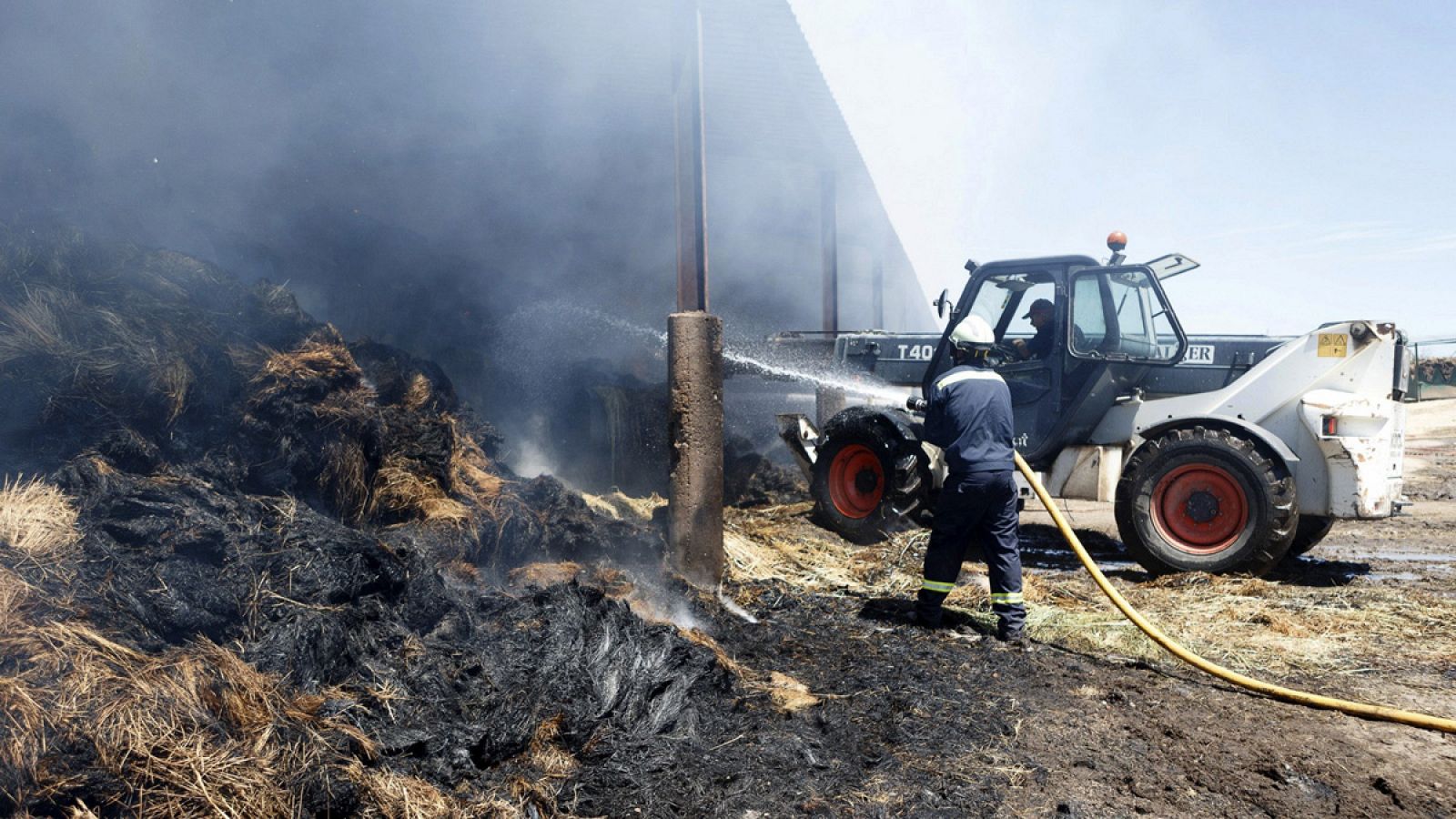 Un bombero refresca varias pacas de paja quemadas en el incendio forestal que se declaró en el entorno del parque natural de Arribes del Duero