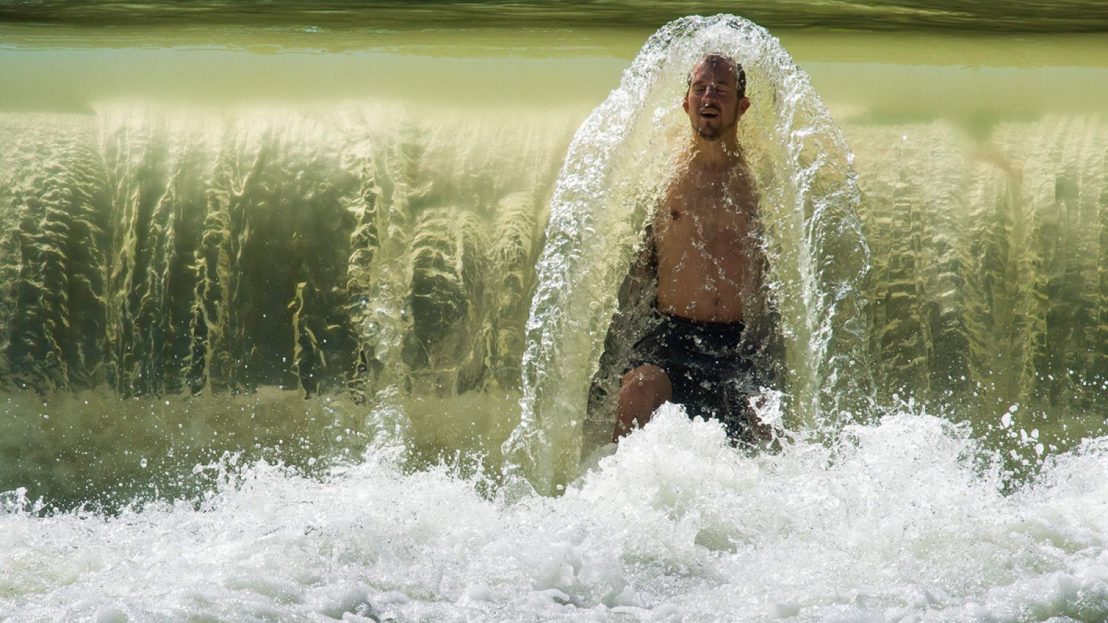 Un hombre se refresca en una pequeña cascada en el arroyo Eisbach, en Múnich