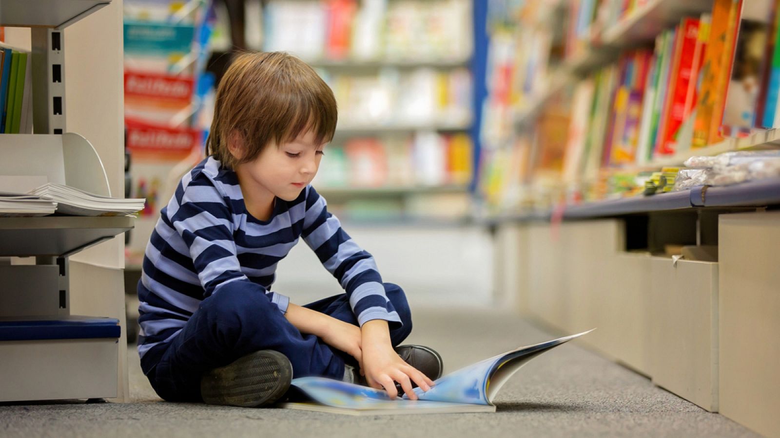 Niño leyendo libros sentado en el suelo de una biblioteca