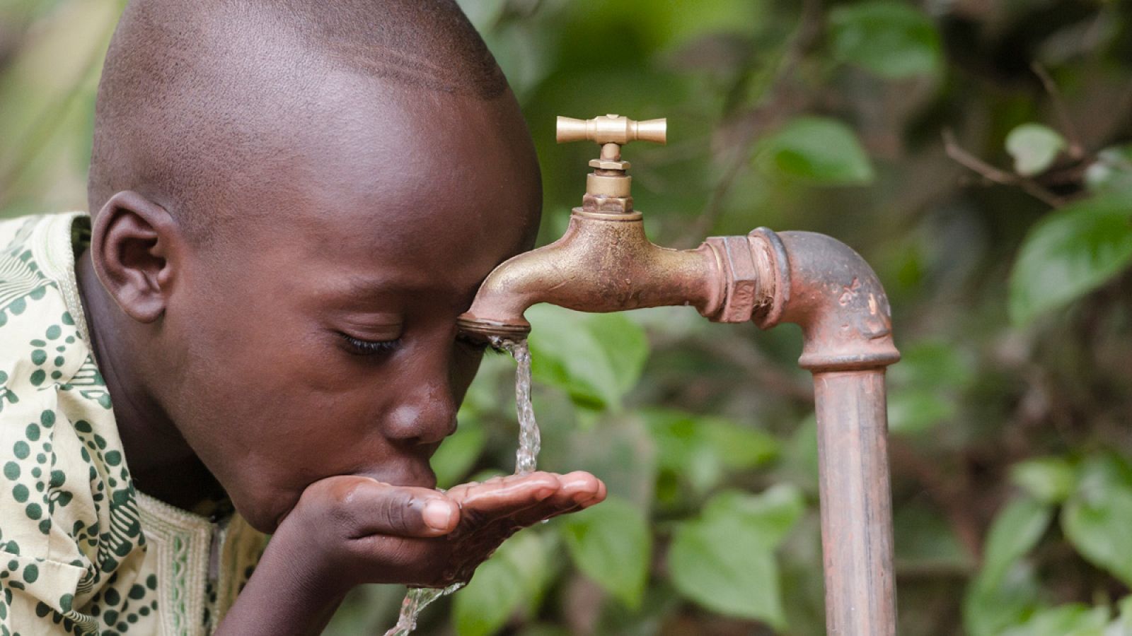 Un niño africano bebe en un grifo agua no potable