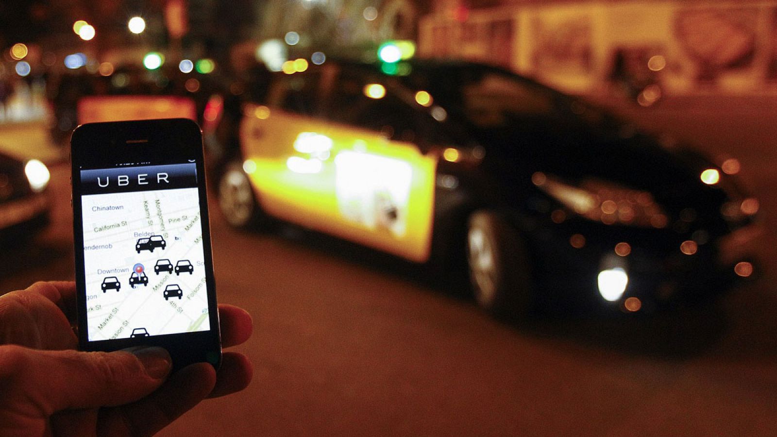 La aplicación para móviles de Uber en un smartphone junto a una cola de personas que esperan para coger un taxi