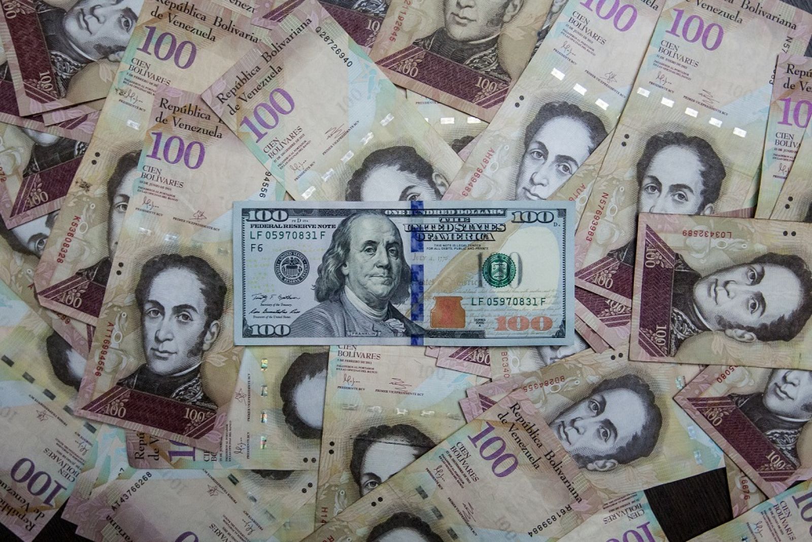 Fotografía de billetes de pesos venezolanos junto a un dólar estadounidense
