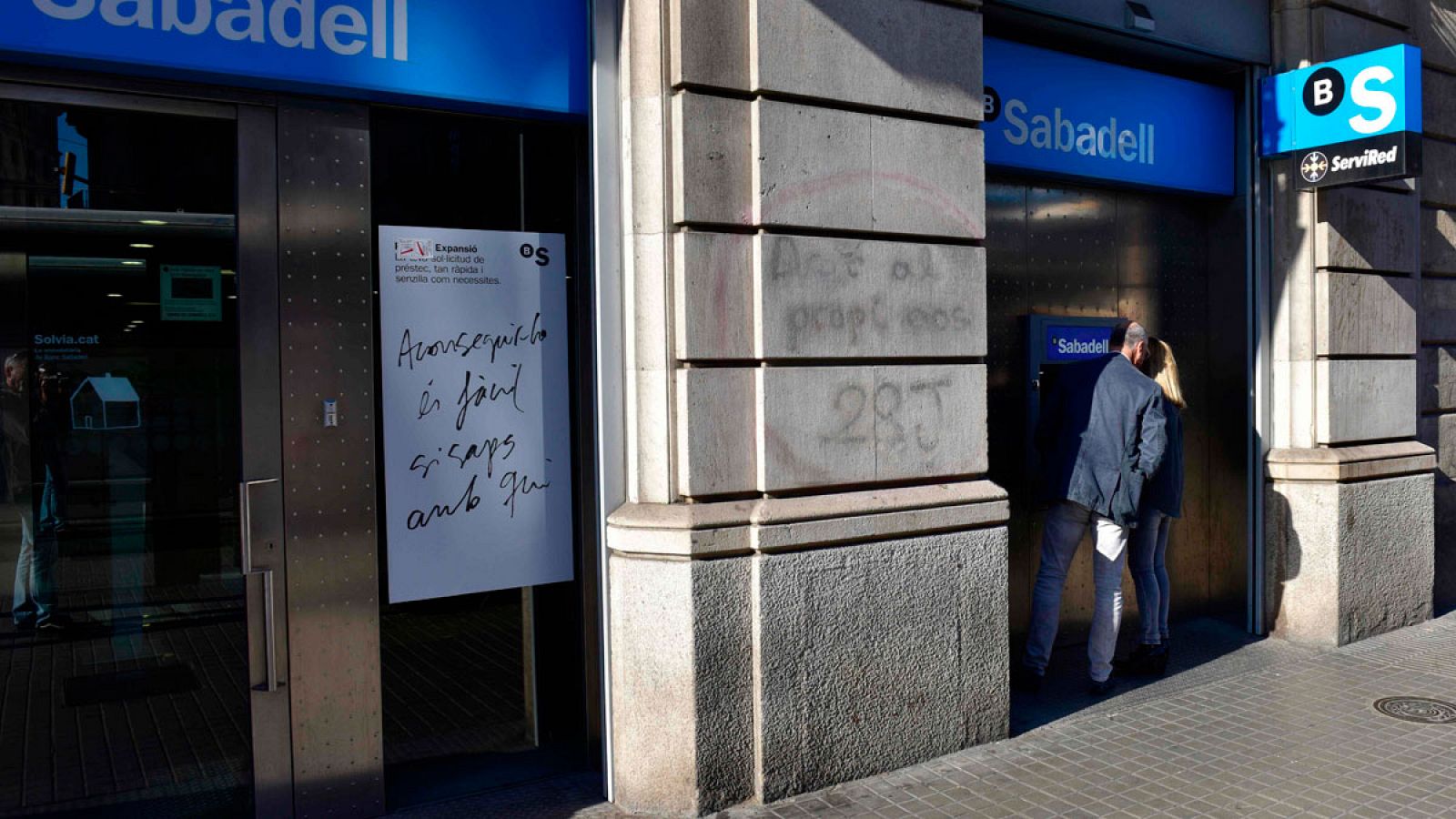 Una pareja retira efectivo de un cajero de Banco Sabadell en el centro de Barcelona