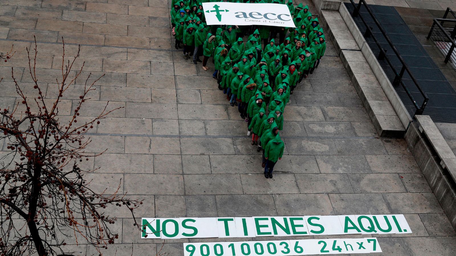 Varias personas vestidas de verde forman el símbolo de ubicación que representa la campaña de la AECC 'Si luchas contra el cáncer, nos tienes aquí'
