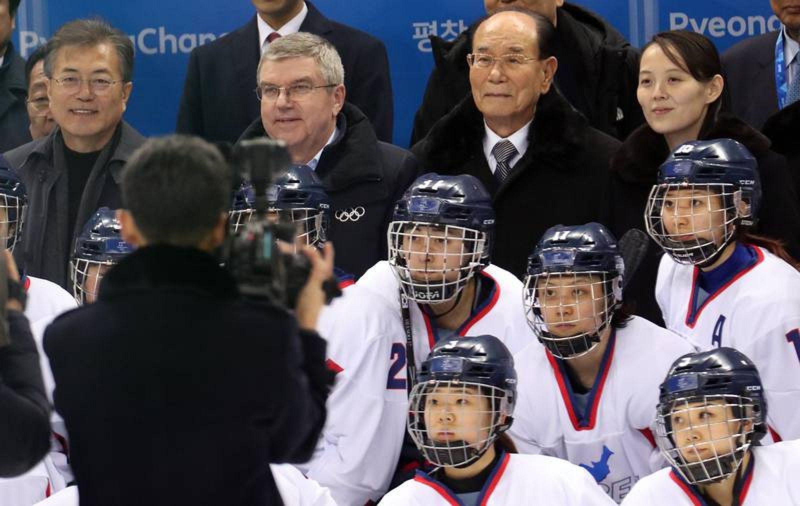 El equipo unificado de Corea de hockey sobre hielo femenino posa con las autoridades de fondo: de izquierda a derecha, el presidente sucoreano Moon Jae-in, el del COI, Thomas Bach; y la hermana del líder  norcoreano y el presidente de su Parlamento, Kim Young-nam y Kim Yo-jong.