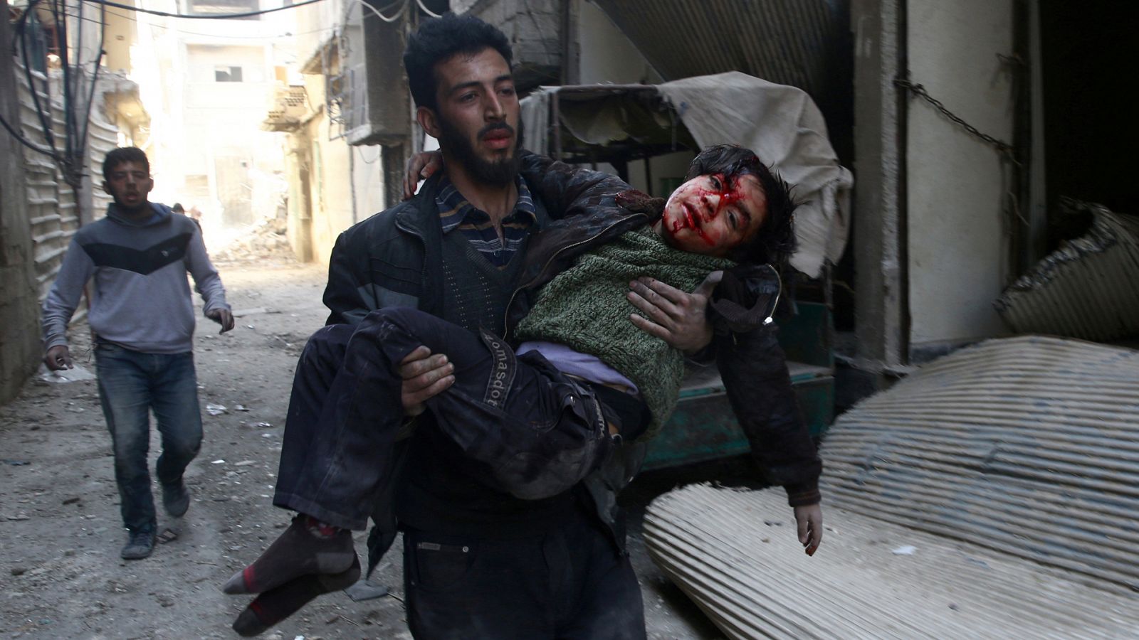 Un hombre corre cargando con el cuerpo de un joven herido en Guta Oriental, cerca de Damasco