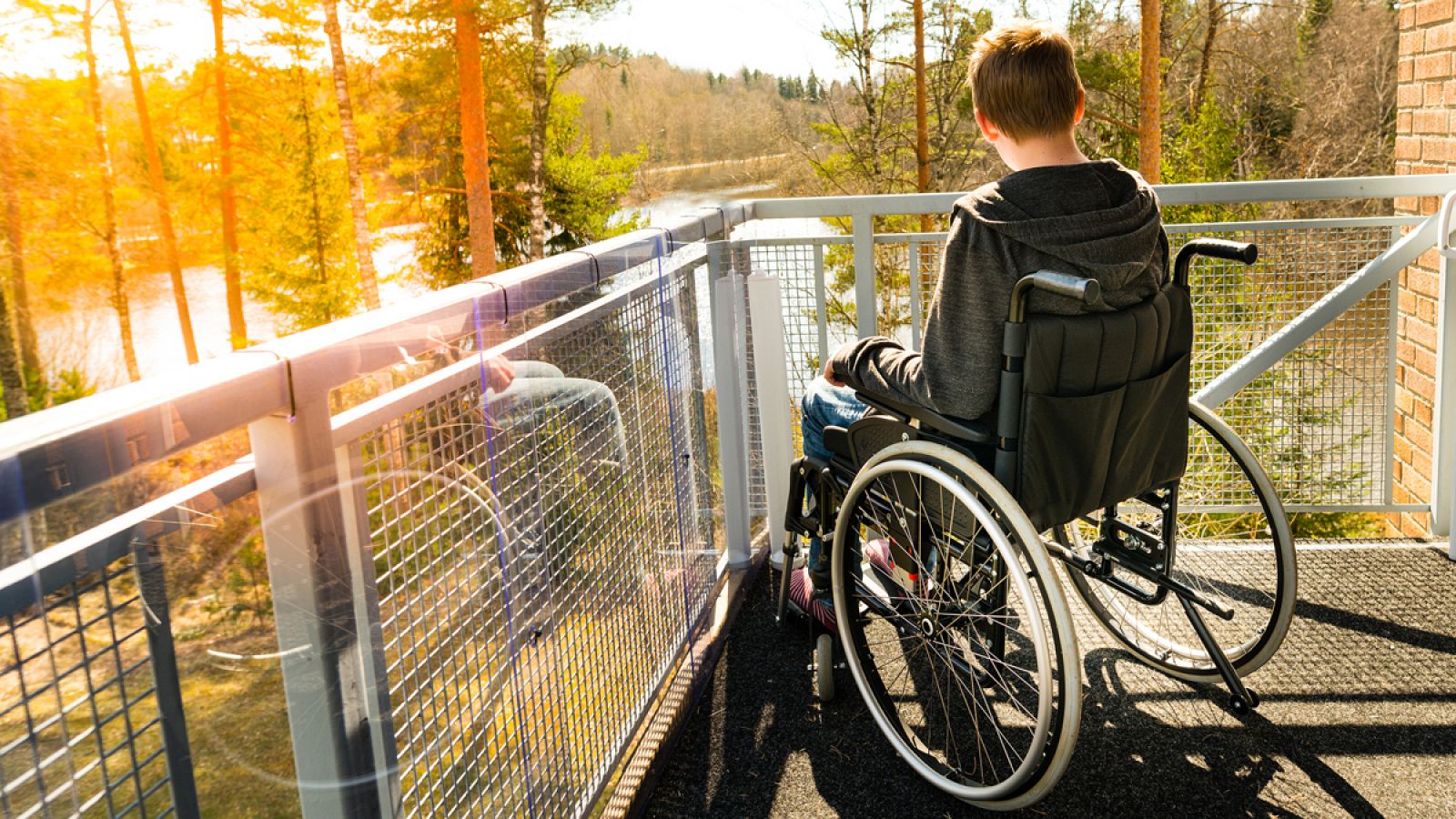 Un muchacho en silla de ruedas mira desde un balcón