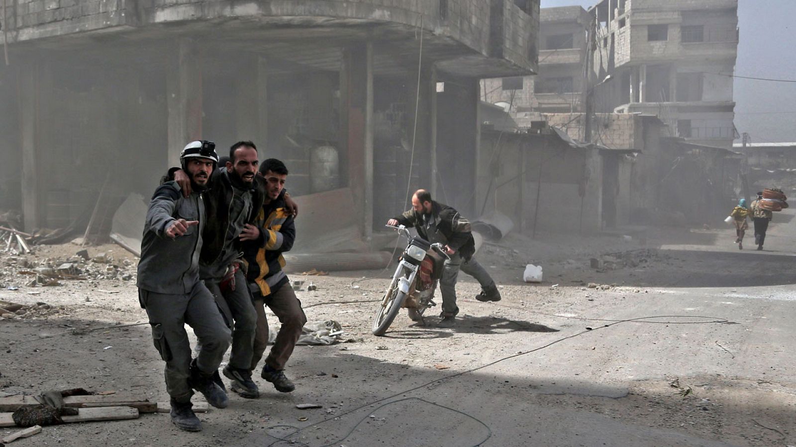 Los voluntarios de los 'cascos blancos' ayudan a un hombre durante un bombardeo en Hamuria, en Guta Oriental