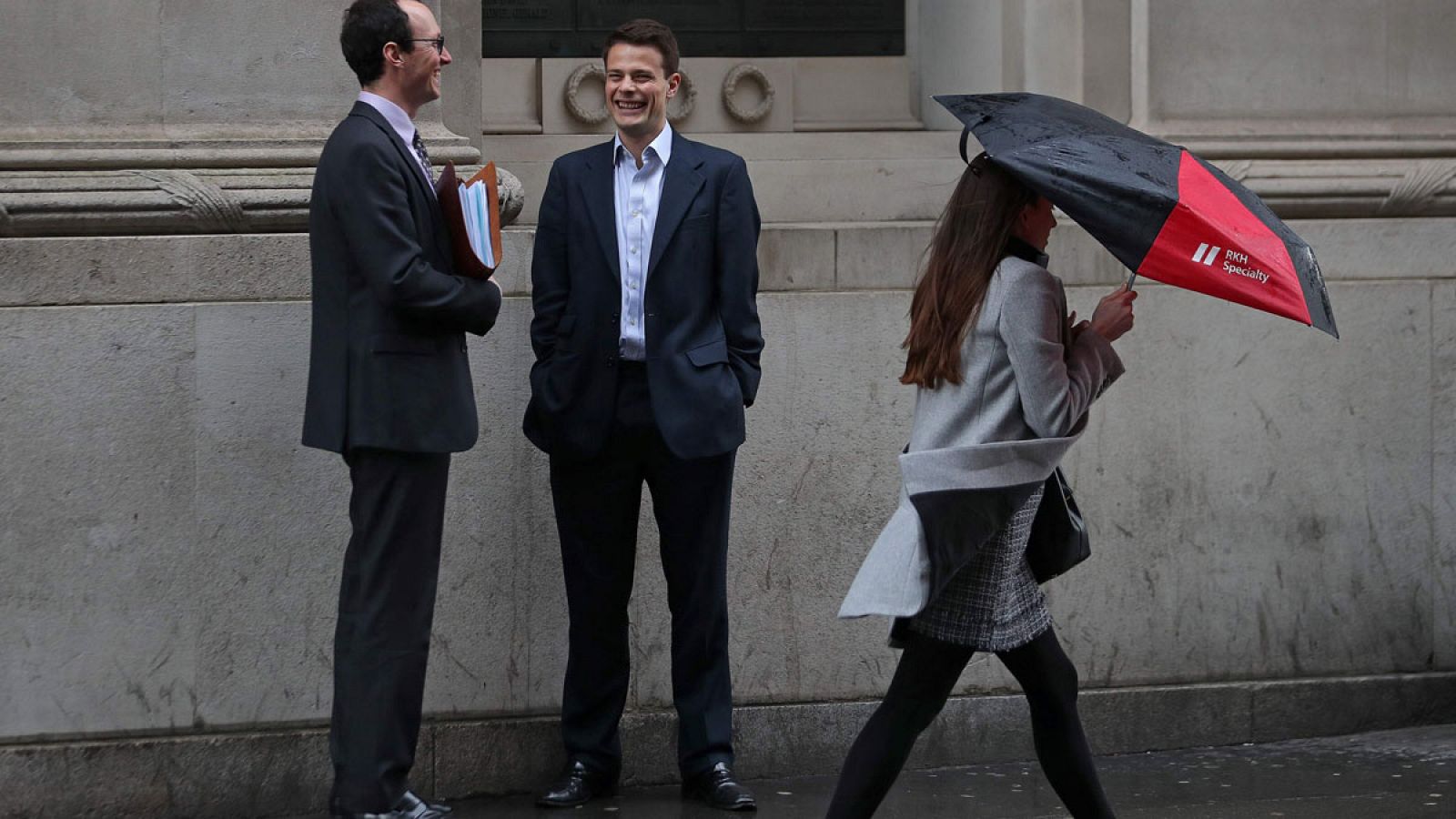 Una mujer se protege con un paraguas mientras camina junto a dos hombres en la City londinense