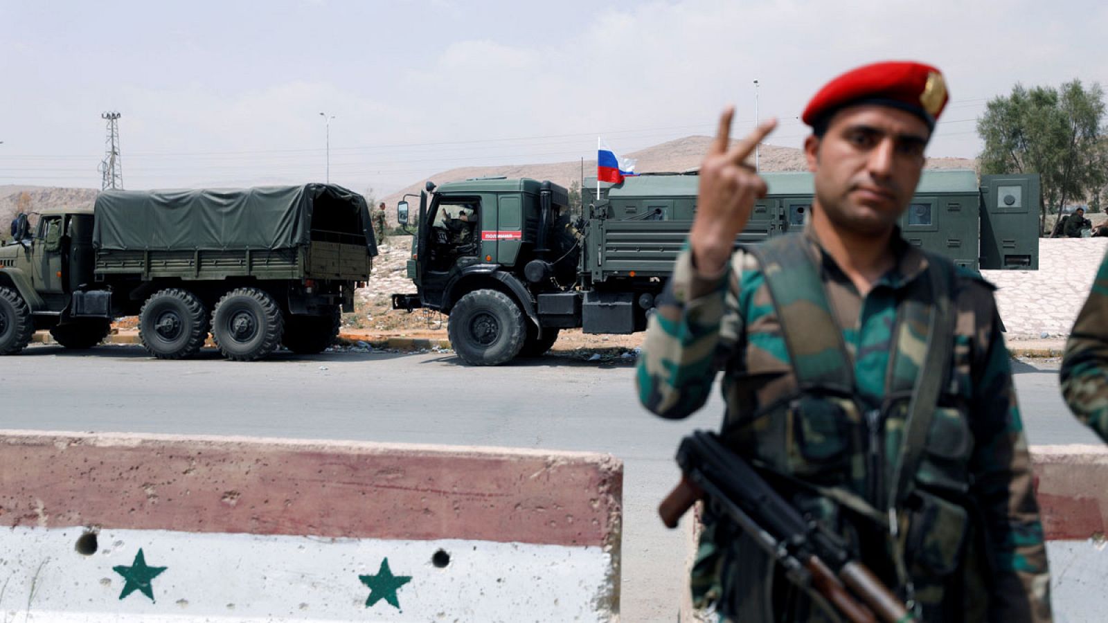Un soldado sirio gesticula delante de un vehículo militar con una bandera rusa.