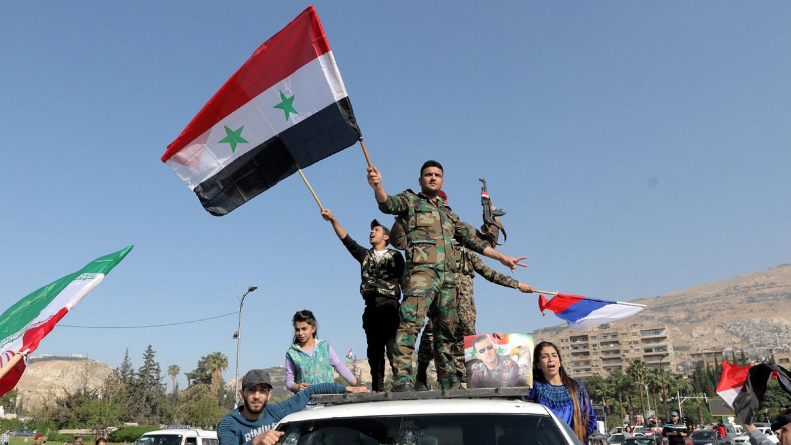 Soldados sirios ondean su bandera nacional junto con las de Irán y Rusia durante una concentración en apoyo al Gobierno sirio celebrada en la plaza de Umayyad en Damasco