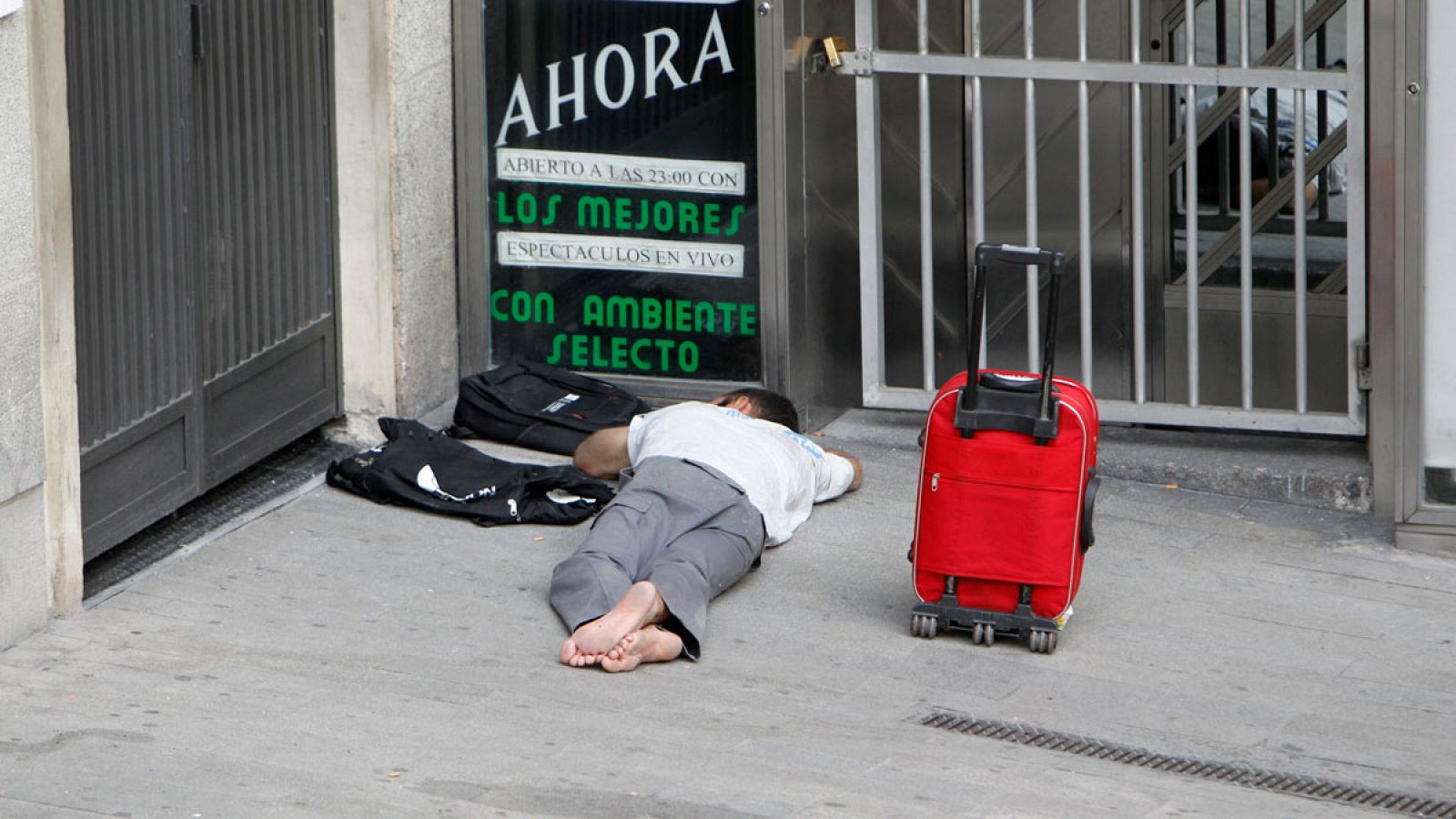 Un indigente, tumbado en el suelo junto a un cartel de una sala de fiestas en Madrid