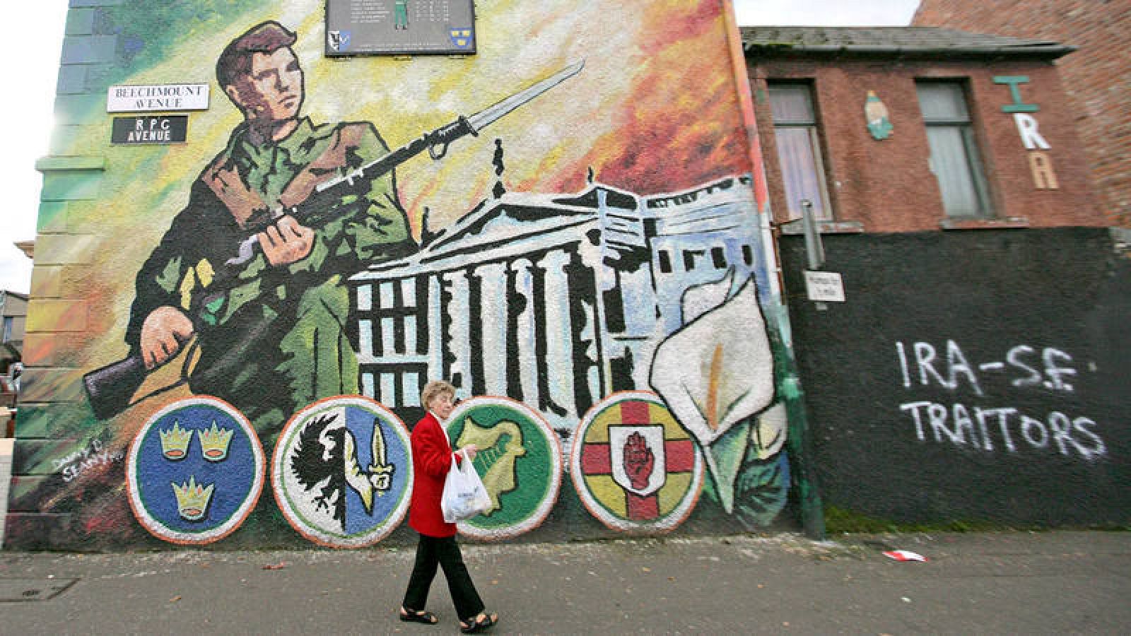 Una mujer pasa ante un mural nacionalista en Belfast, junto a una pintada que califica de "traidores" al IRA y al Sinn Féin