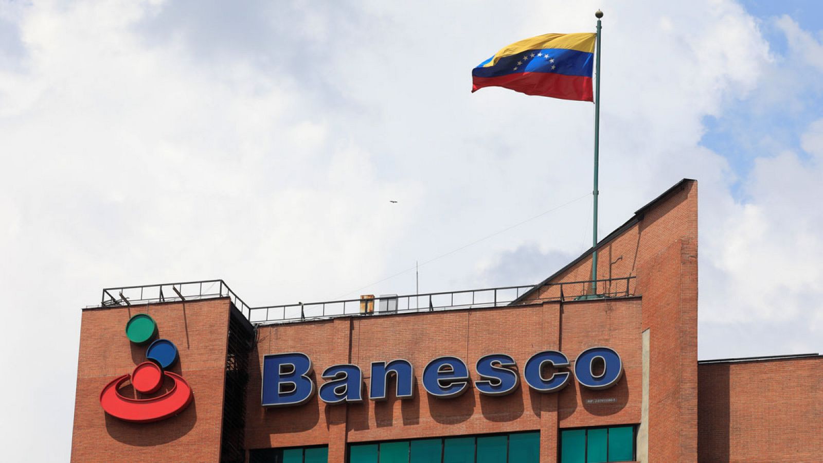 Una bandera venezolana ondea sobre el logotipo corporativo del banco Banesco en uno de sus complejos de oficinas en Caracas, Venezuela