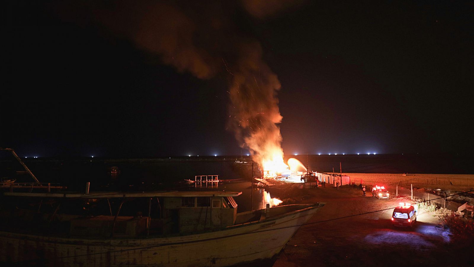 Bomberos palestinos inspeccionan un barco de pesca en llamas en el puerto de Gaza