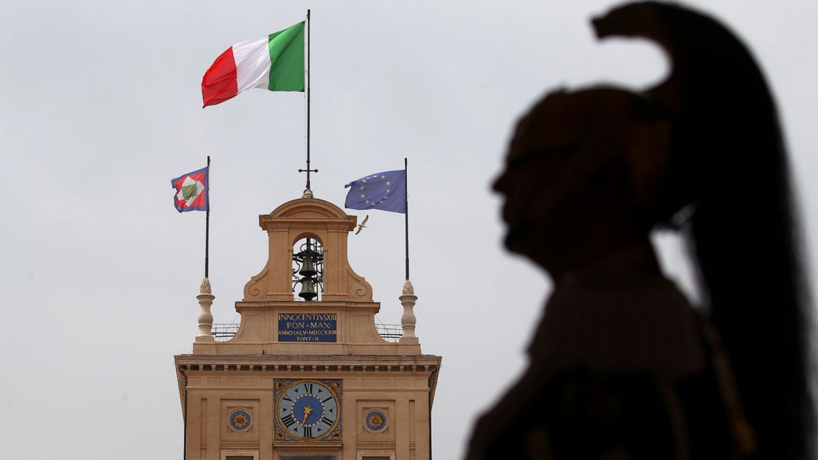 La sombra de un guardia del Quirinal se perfila junto a las banderas que ondean en la sede de la Presidencia italiana