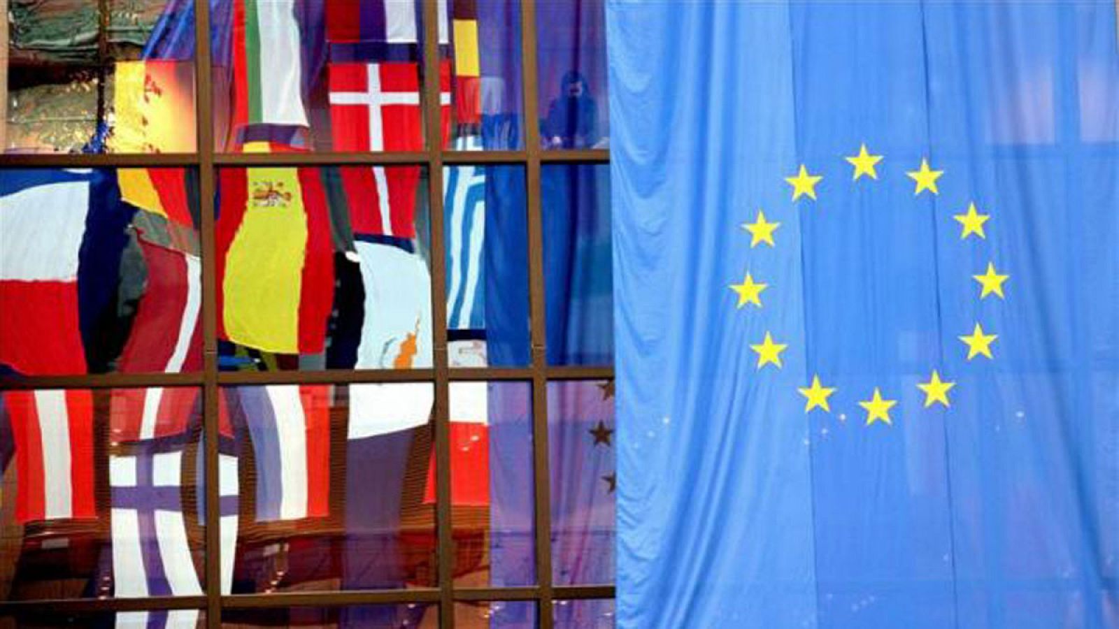 Reflejo en una cristalera de las banderas de miembros de la UE junto a una enseña europea