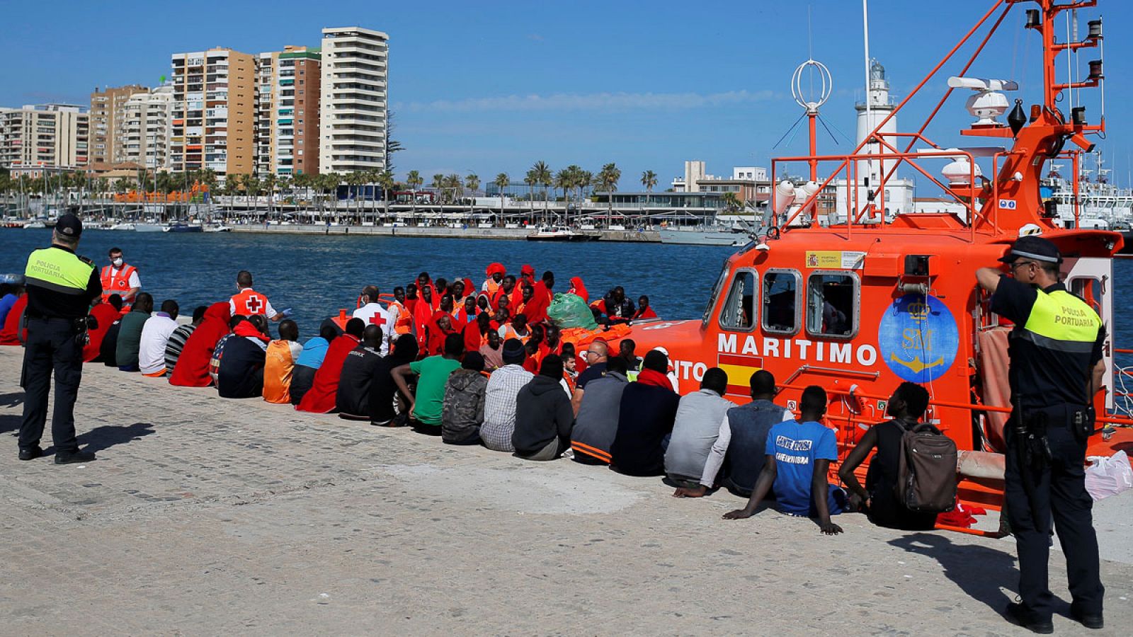 Un grupo de inmigrantes espera en el puerto de Málaga junto al barco que les rescató