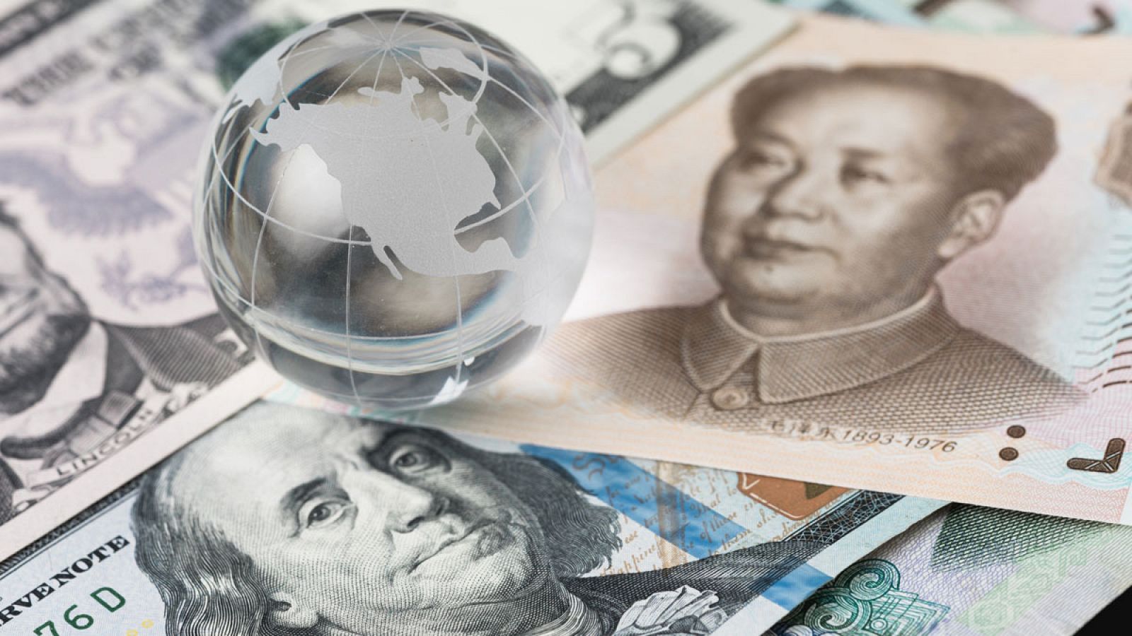 Un globo terráqueo de cristal sobre billetes de dólar y yuan