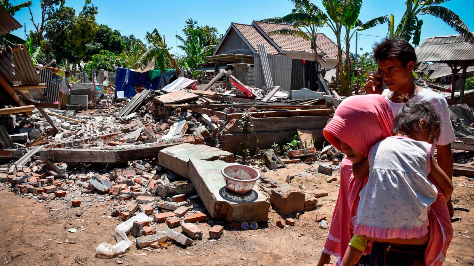 Una mujer carga a su hijo mientras atraviesan las casas derrumbadas en el pueblo de Sugar, en la isla indonesia de Lombok.