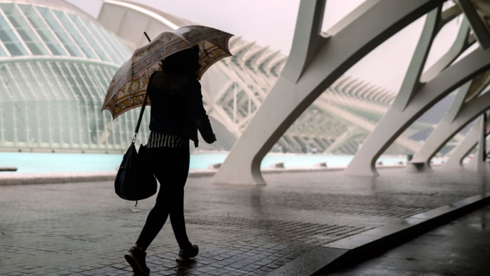Una persona se resguarda de la lluvia en la Ciudad de las Ciencias de Valencia