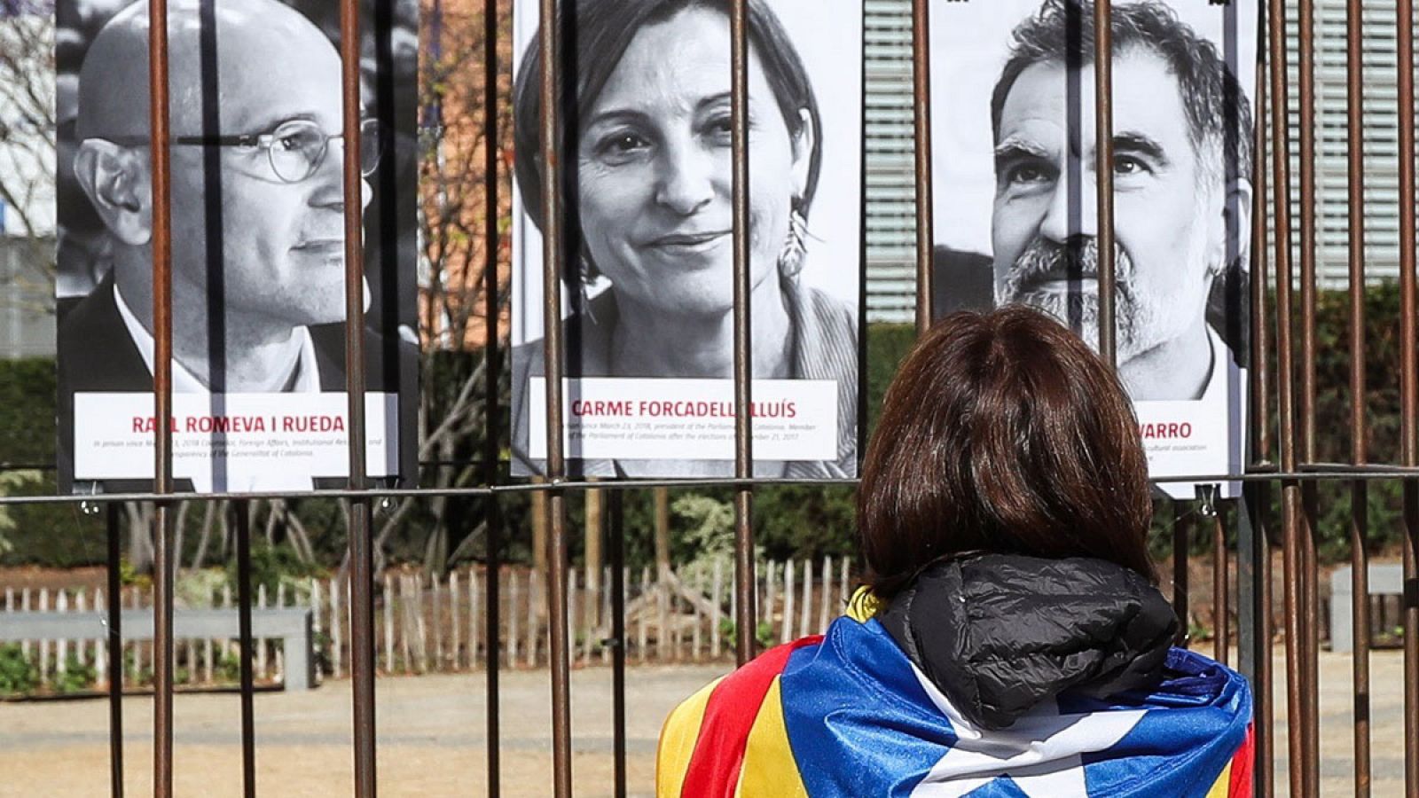 Una personas envuelta con la enseña catalana mira carteles de políticos encarcelados