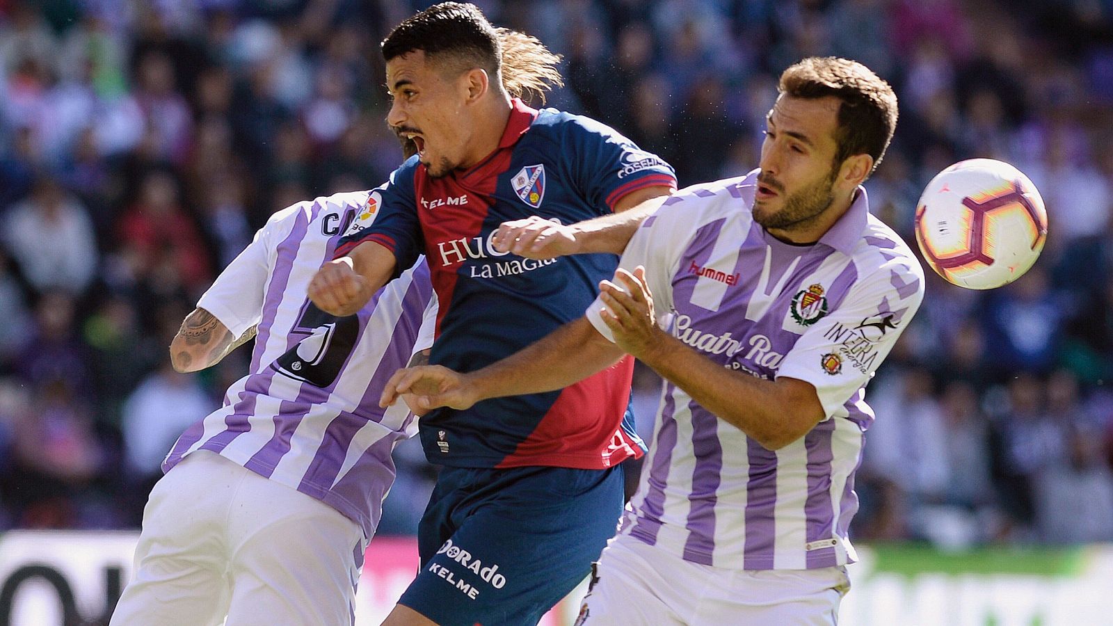 El centrocampista turco del Huesca, Serdar Gürler, pugna por un balón aéreo con los jugadores del Real Valladolid, Fernando Calero, y Francisco Olivas.